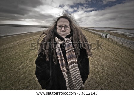 Woman in black coat and with scarf on Germen dike close to tidal water.