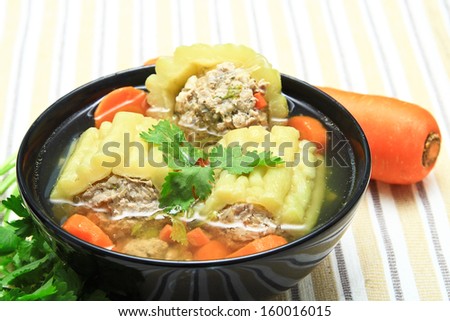 Pork soup with bitter gourd and carrot in black bowl.