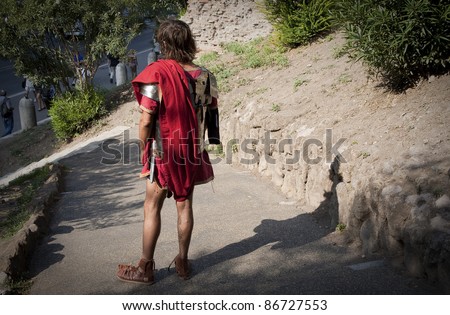 Street performer dressed like Roman soldier offer photo sessions to tourists in a park near Colosseum, Rome.