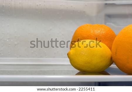 A lemon and two oranges inside fridge, sitting alone on the shelf. Copyspace provided.