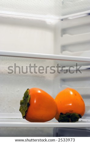 Two persimmons inside fridge, sitting alone on the shelf. Copyspace provided.