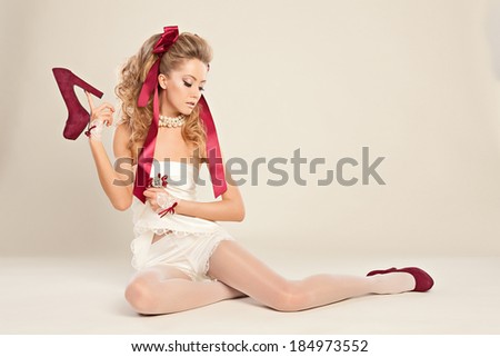 Young woman  in the doll style with red bow and red shoes  sitting on the floor. Studio photography .