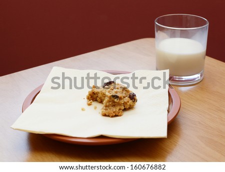 Half-eaten oatmeal raisin cookie with a half drunk glass of milk