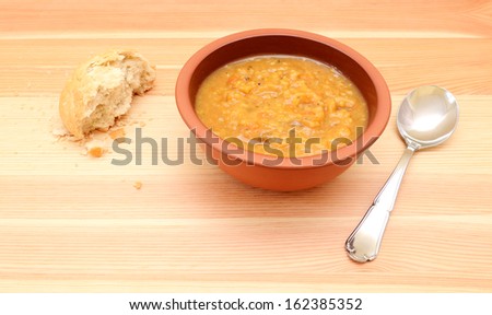 Half-eaten crusty bread roll with a bowl of chunky vegetable soup