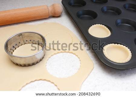 Lining a bun tin with circles of rolled out pastry to make mince pies, with a rolling pin on the worktop