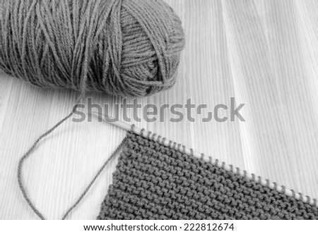 Close up of ball of wool with length of garter stitch on a knitting needle, on wood - monochrome processing