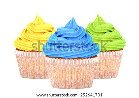 Three cupcakes with colorful yellow, blue and green frosting isolated on a white background