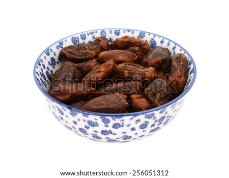 Whole dates in a blue and white porcelain bowl with a floral design, isolated on a white background
