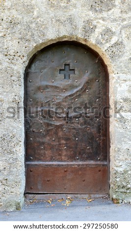 Old studded metal door, decorated with a cross and engraving, in a stone wall in Salzburg, Austria
