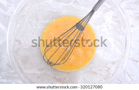 Wire balloon whisk in a glass bowl of beaten eggs on a kitchen work surface