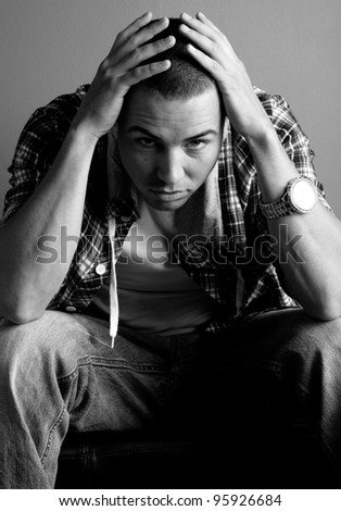 Moody photo of young man sitting with head in hands looking unhappy.