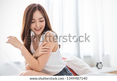 Portrait of beauty  smiling asian woman applying a lotion to her arm skin during her morning routine. Cute asian girl. Skincare body lotion, beauty clinic skincare spa indoors woman lifestyle concept