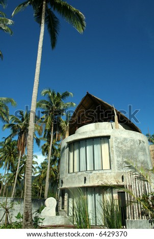 Modern house near tropical beach with palm trees and blues sky background.