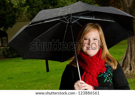 smiling woman wearing a red scarf and holding an umbrella on a rainy day.