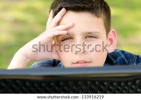 a 10 year old boy with his hand on his head as he looks over the lap top computer screen.