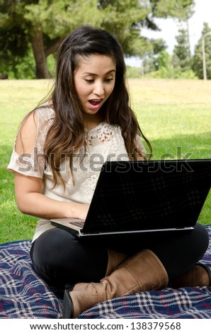 A woman in the park with a surprised look on her face as she looks at her computer.