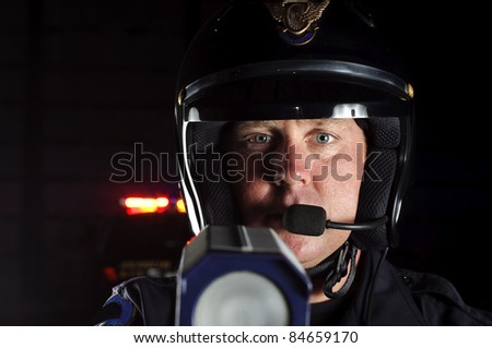 a police officer at night pointing his radar gun at traffic.