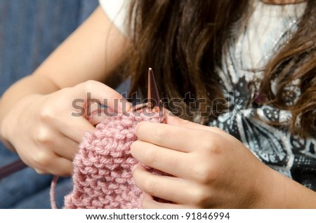 a 7 year old little girl sits on the couch as she learns to knit.