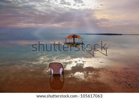 A stunning visual effect on the Dead Sea. Sun rays and picturesque gazebo for bathersare are reflected in a smooth sea surface.