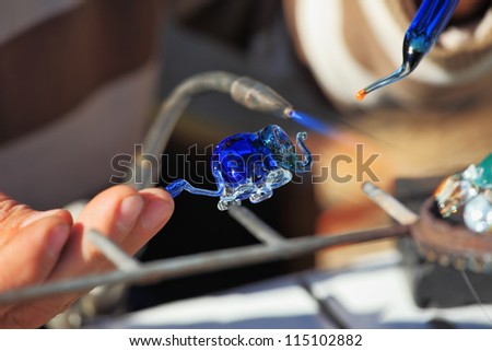 Delicate work of the glass blower. The Artist-glass blower produces a graceful tiny figure of an elephant from color glass. On a photo hands of the master are visible