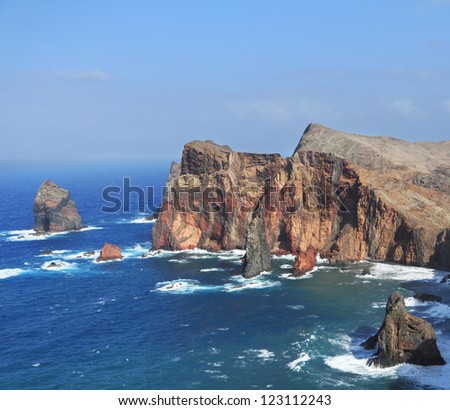 Windy day on ocean island Madiera. Bright red and gray coastal rocks of east part of island