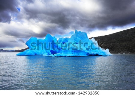 The harmony of the iceberg and cold water. Patagonia in the clouds and sunshine. Blue ice iceberg reflected in the lake Gray