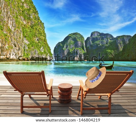 Cozy beach rest. Two wooden chaise lounges and small bedside table. Through emerald sea water thin yellow sand is visible