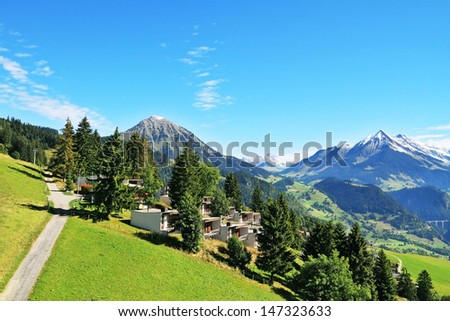 Magnificent Swiss Alps in early fall. Road among green alpine meadows leading to the mountain chalet The picturesque alpine meadows, rural houses chalets