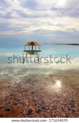 Medical beach on the Dead Sea, Israel. Round gazebo in the water near the water\'s edge. Cloudy sky reflected in water