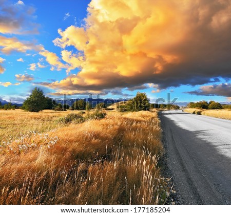 Gravel road through the Patagonian steppe in Argentina. The huge cloud lit yellow-orange rays of sunset