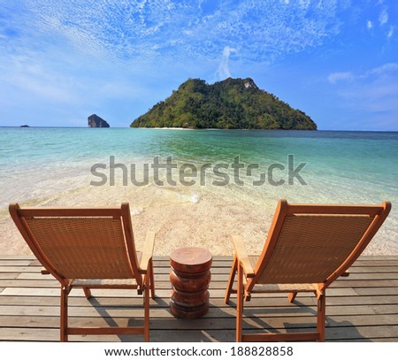 Romantic corner on the beach. Two folding wooden chairs and a small side table. Through the emerald sea water visible fine yellow sand