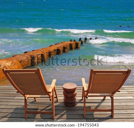 Comfortable lounge chairs on wooden platform for rest and observation. Breakwater of the emerald sea waves