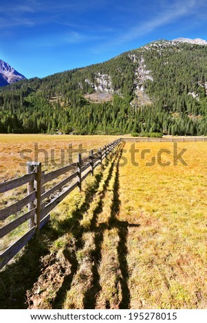 Alpine Valley in Austria. National Park Krimml. Scenic farm fields blocked bythe wooden fence. Shadow of the low fence beautifully lie on the grass.