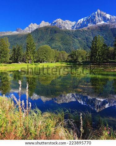 Snowy mountains and evergreen forests in the famous mountain resort of Chamonix. Gorgeous reflection in the smooth water of the lake in the park