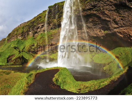 Seljalandsfoss waterfall in Iceland. Summer sunny day. Large rainbow decorates a drop of water. The picture was taken Fisheye lens