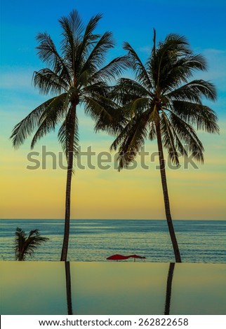 Palm trees reflected in smooth water of the pool on the beach. Delicate sunset on the popular resort island of Koh Samui