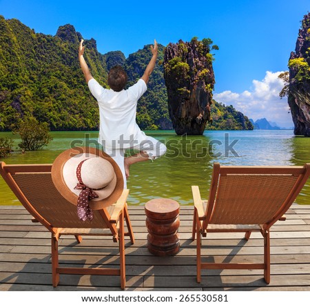 Exotic vacation in Thailand. Two beach chairs and an elegant hat on one. Woman performs yoga pose \