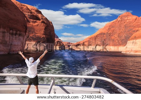 Man in  white shirt on the stern boat fascinated by nature. Artificial lake Powell on the Colorado River, USA. The lake is surrounded by picturesque beaches of the orange sandstone