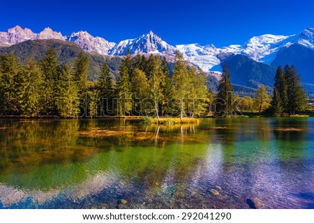The snow-covered Alps and evergreen fir-trees are reflected in lake. Early fall in Chamonix, Haute-Savoie. France