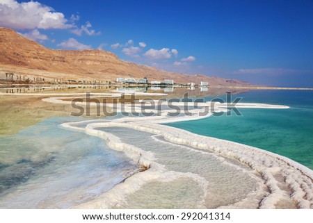 Israeli coast of the Dead Sea. Path from the salt winds picturesquely in salt water. Hotels on the bank are reflected in smooth water