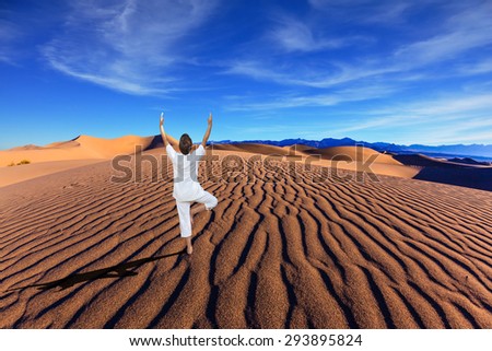 Yoga in the desert. Orange sand dunes in Death Valley, California. A middle-aged woman in a white performs asana \