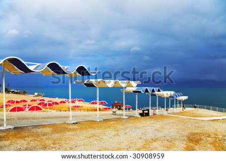 Red beach umbrellas on empty deserted deserted coast of the Dead Sea in a thunder-storm