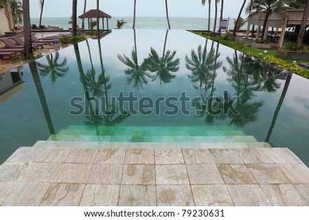 Wide marble steps go down in pool. Smooth water of pool reflects high picturesque palm trees in a beach of Andaman sea