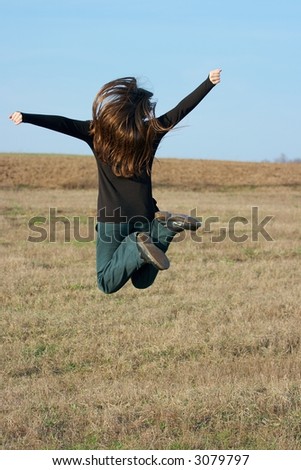 Happy girl jumping around on a dry field