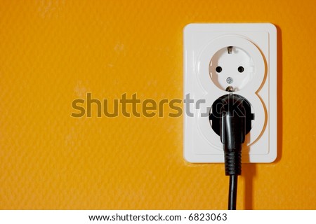 Electric socket with a connected plug on orange wall