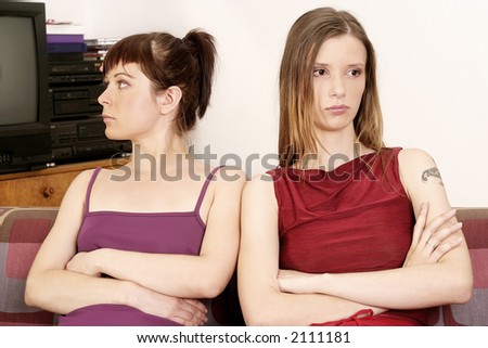 two girls young women sitting on a sofa, looking opposite direction
