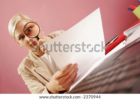 work environment- woman with a magnifying glass over some paperwork in modern office-on pink