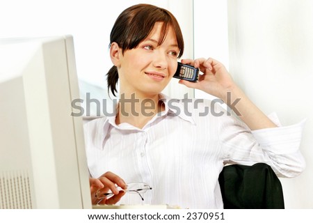 young woman at workplace in front of computer writing in agenda