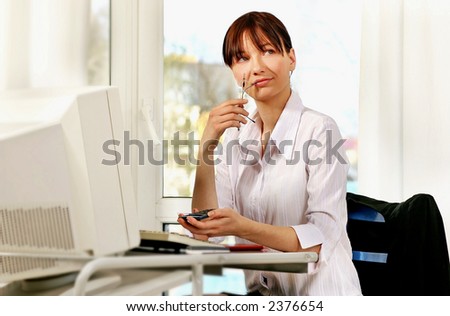 young woman at workplace in front of computer writing in agenda