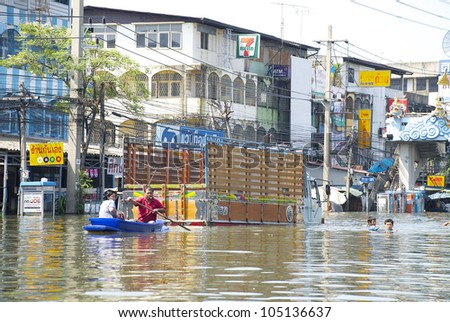 PATHUM THANI, THAILAND - OCT 27: Thai people moving through flood waters on a road in Pathum Thani, using boats or wading to get through the flood, near Bangkok, Thailand on October 27, 2011.